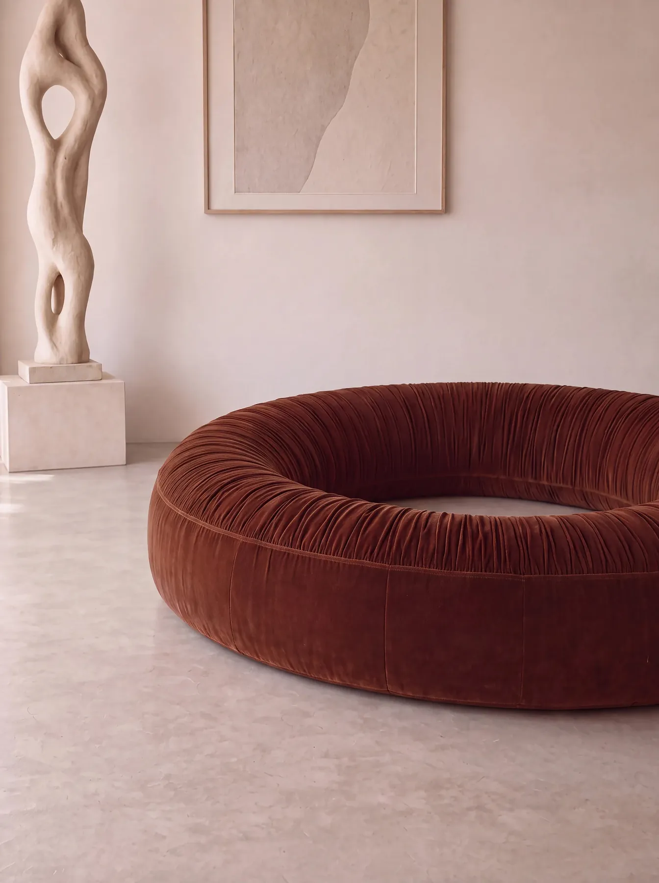 Donut Seat, a terracotta ruched velvet ring, in front of a pale sculpture and wall